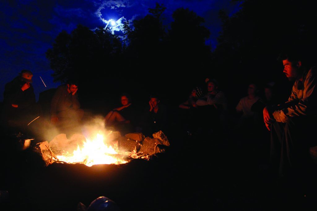 Students gather around a fire discussing the day.