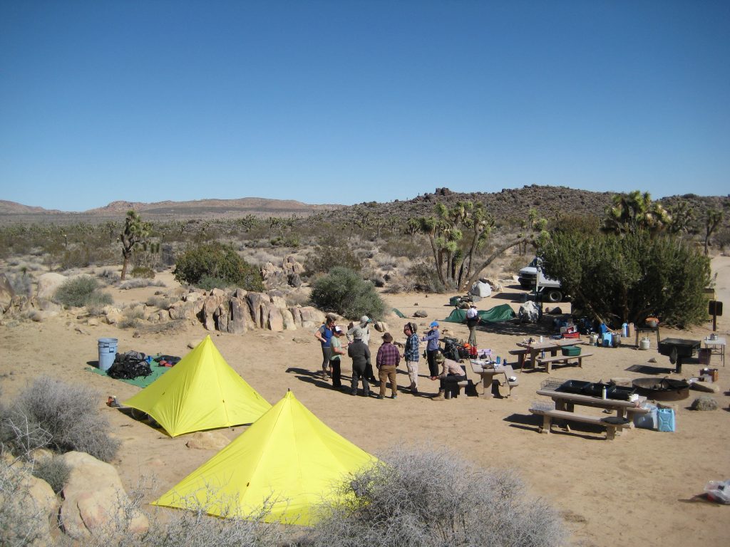 A crew gathers together at their campsite to make a plan for what to do next at their campsite.