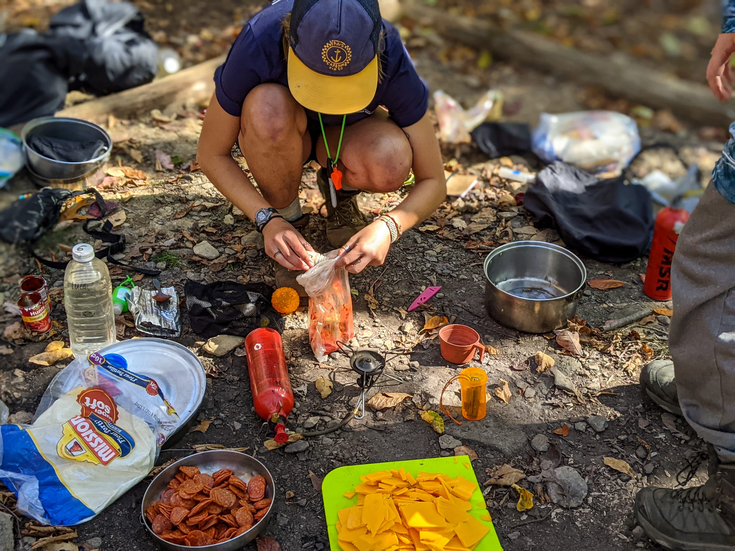 How Outward Bound is Different from Summer Camp: A student prepares a meal outside on the ground near a camp stove.