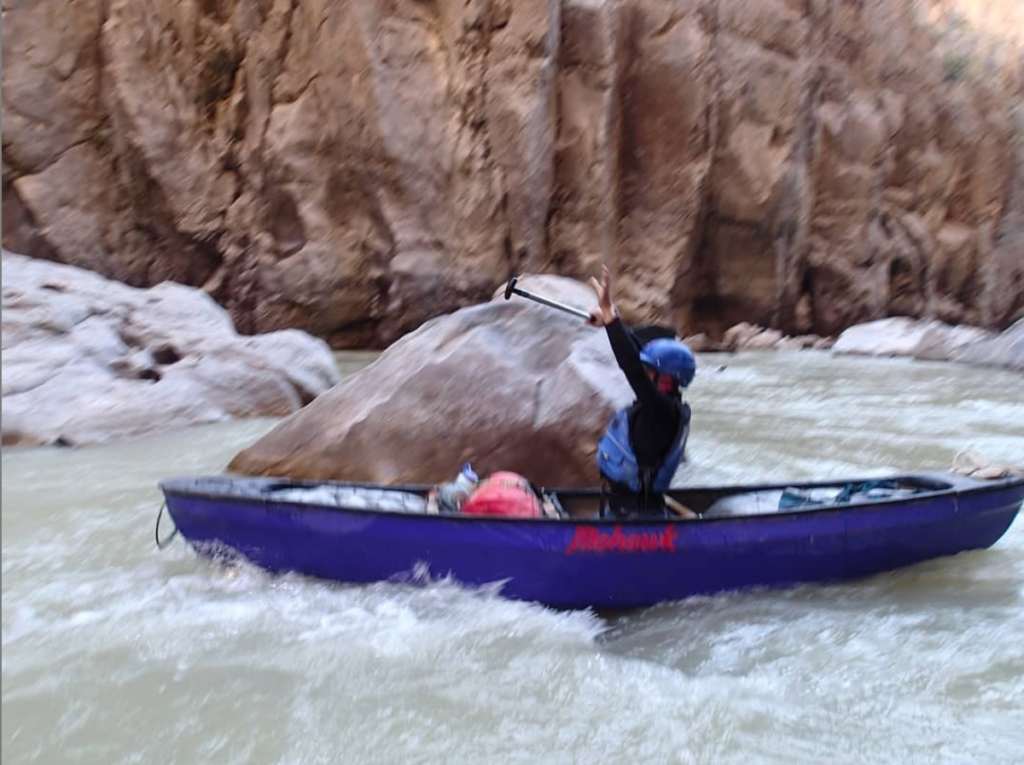 A student uses strength and confidence to put their hands up in a canoe while going through a rapid.