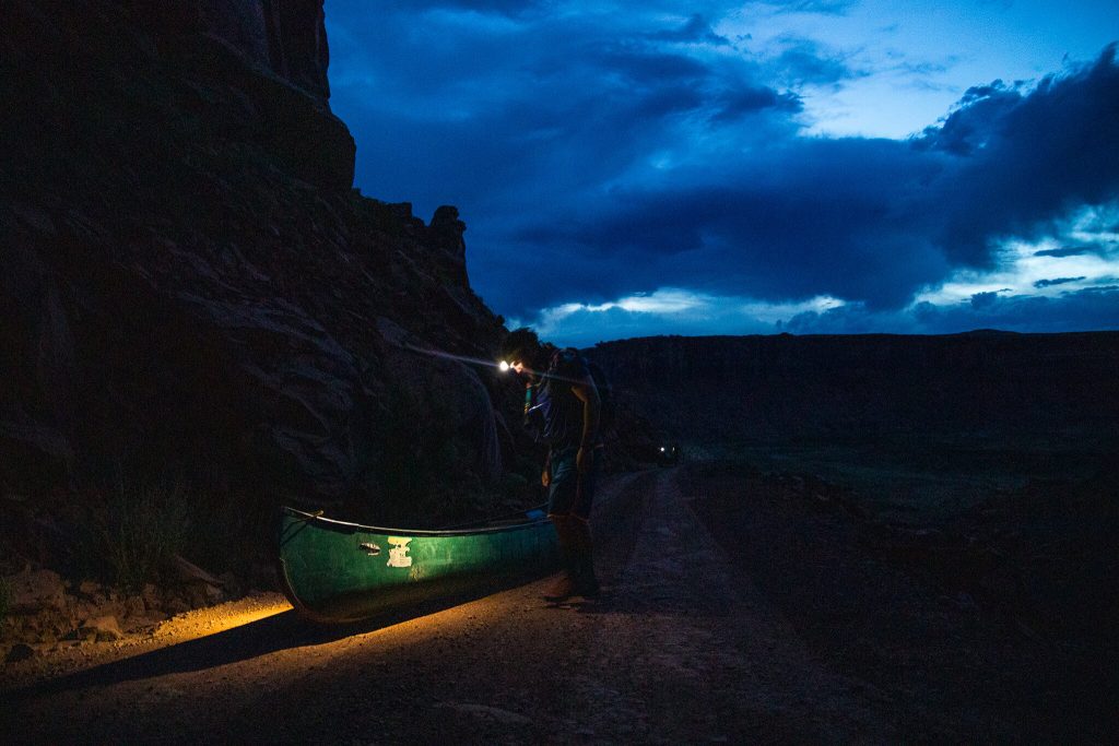 A student looks down on a canoe with a headlamp turned on during dusk.