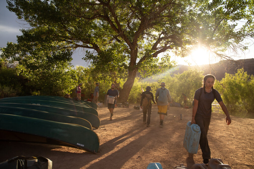 Students carrying gear on a sandy Southwest shore.