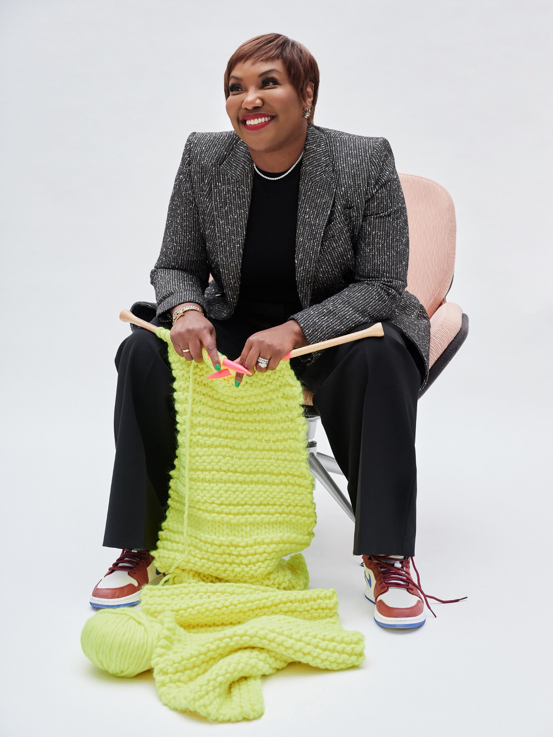 Amani Duncan sitting on a chair and knitting with yellow yarn
