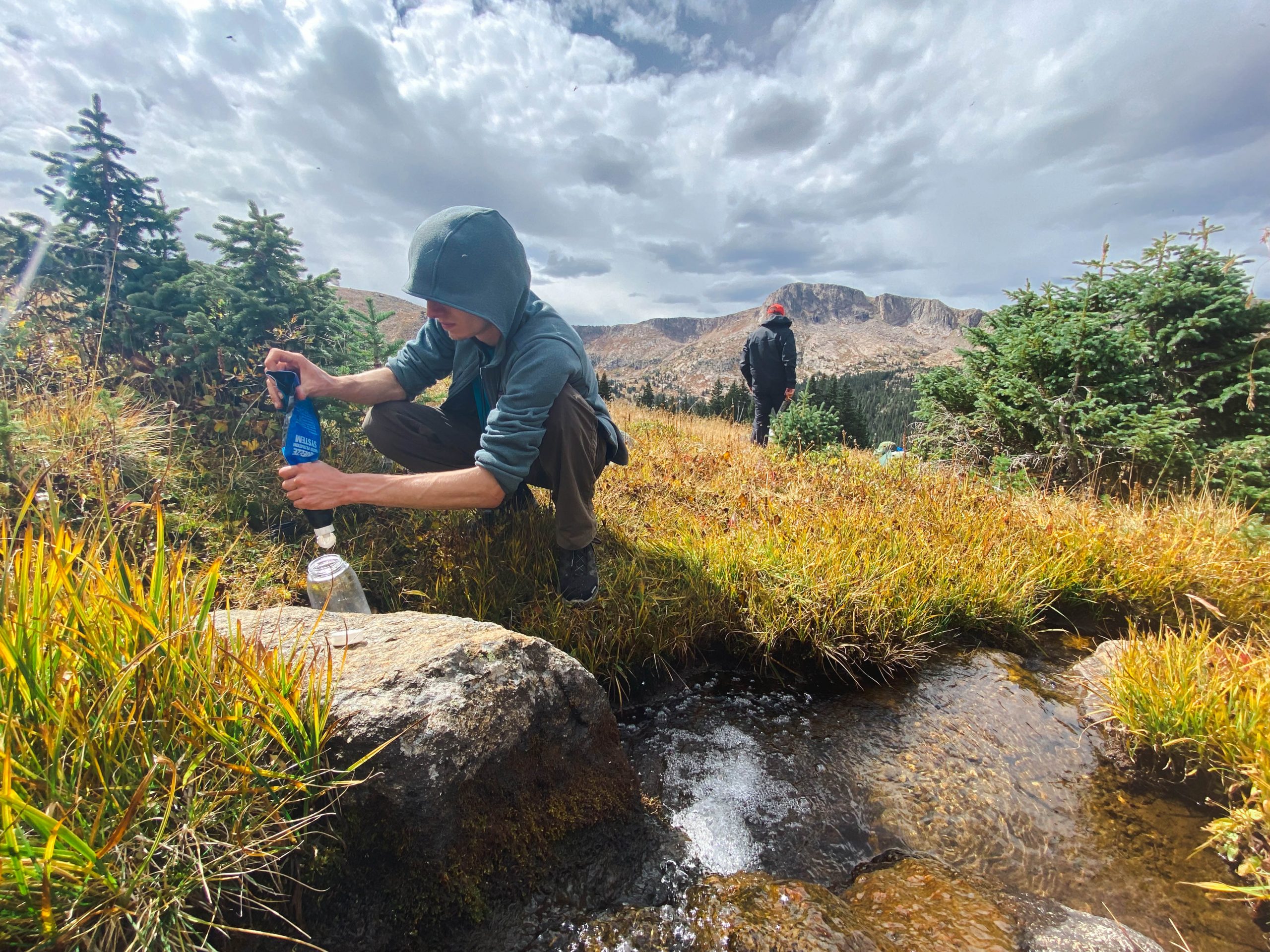 An individual fills up water from a river as they prioritize self-care in the outdoors.