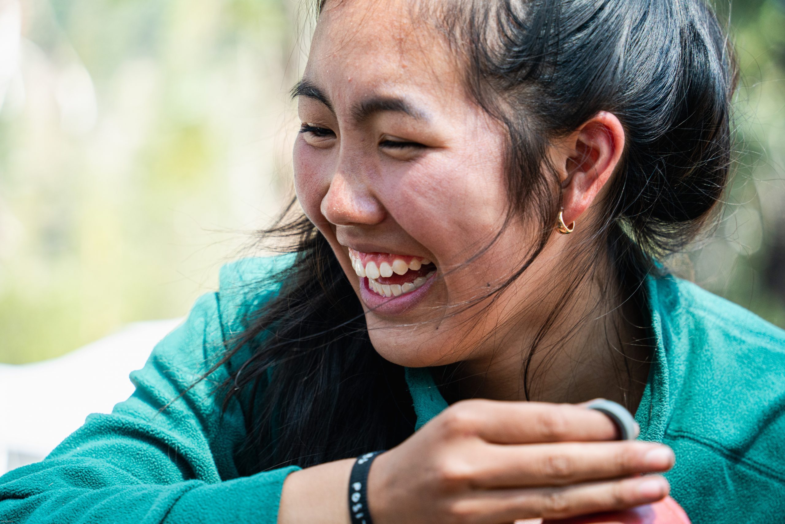 an individual in a green long sleeve smiles as they laugh.