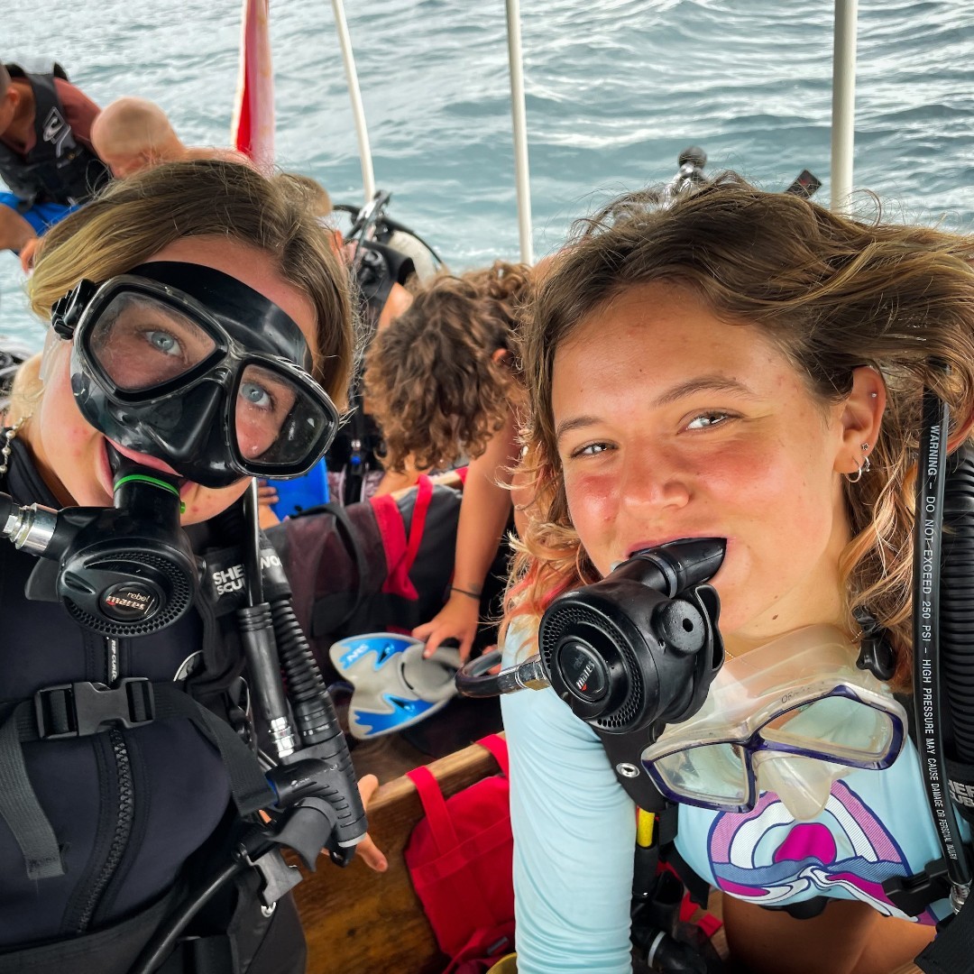 two gap year students on a boat in water smile with scuba gear on.