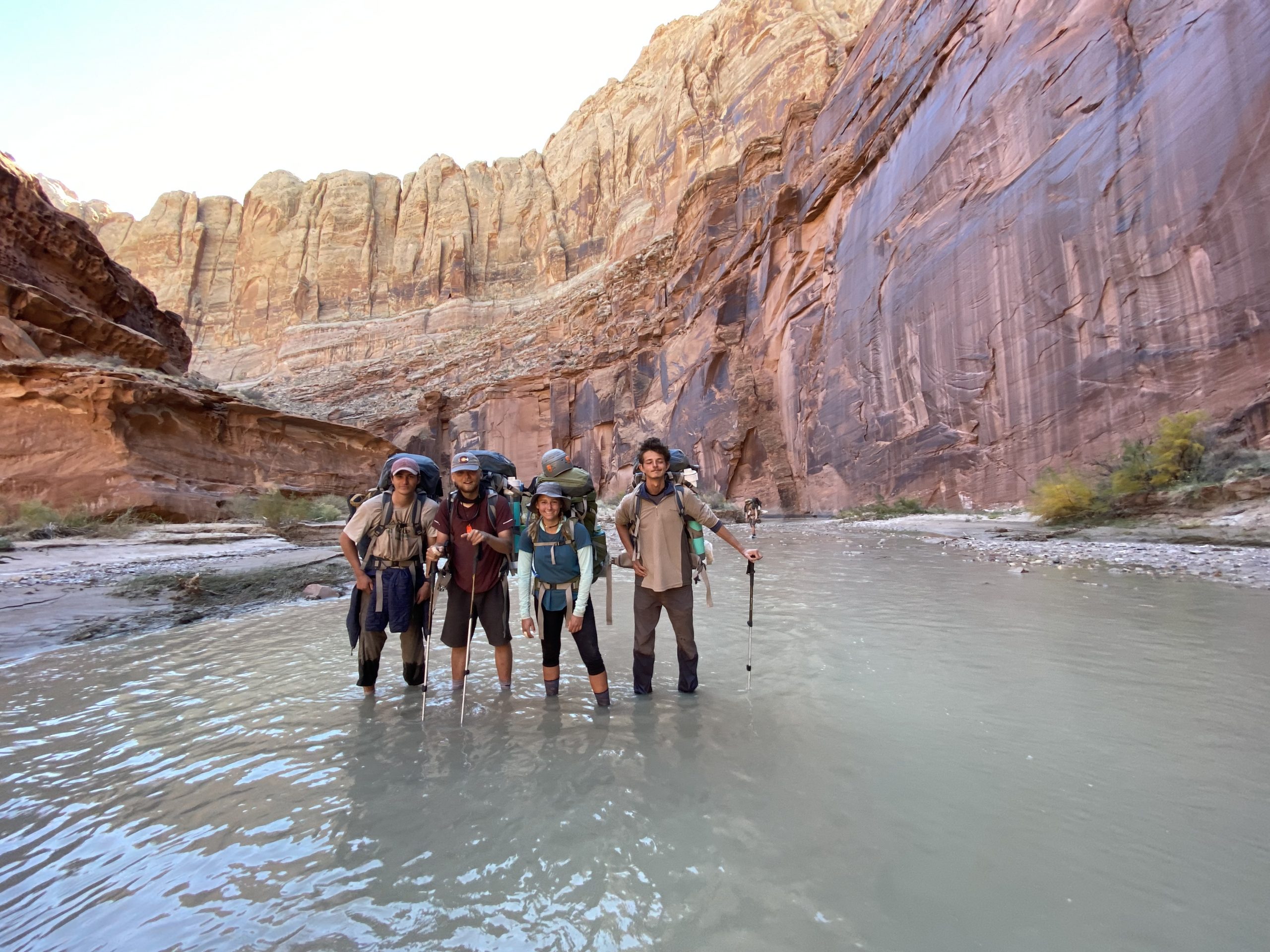 gap year students on semester expedition in utah hike through water in a canyon with backpacks on.