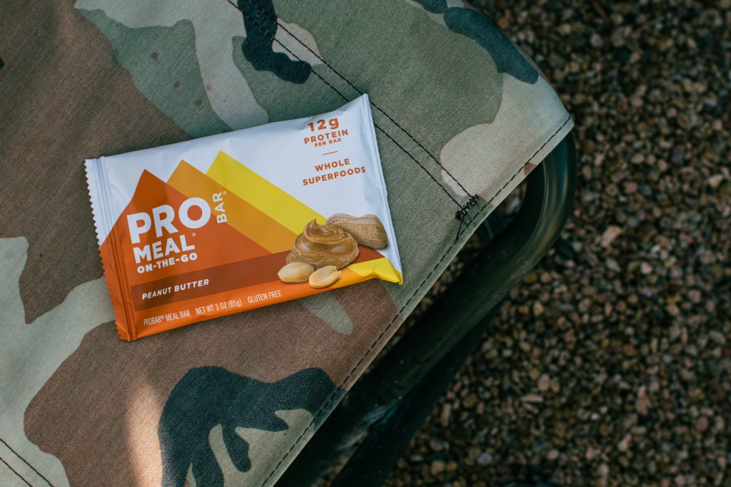 a picture of a protein bar sitting on a camp camp chair outside in a pebbly area.