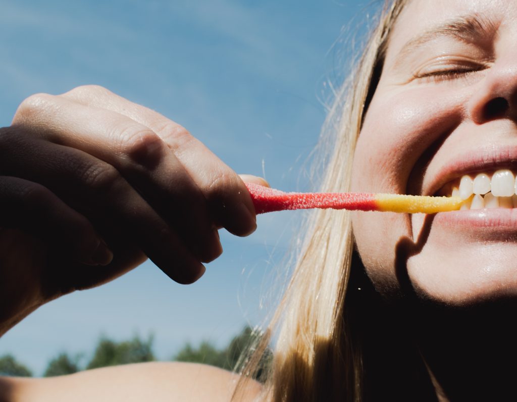 close up of someone biting a gummy worm candy outside. hiking snacks photo.