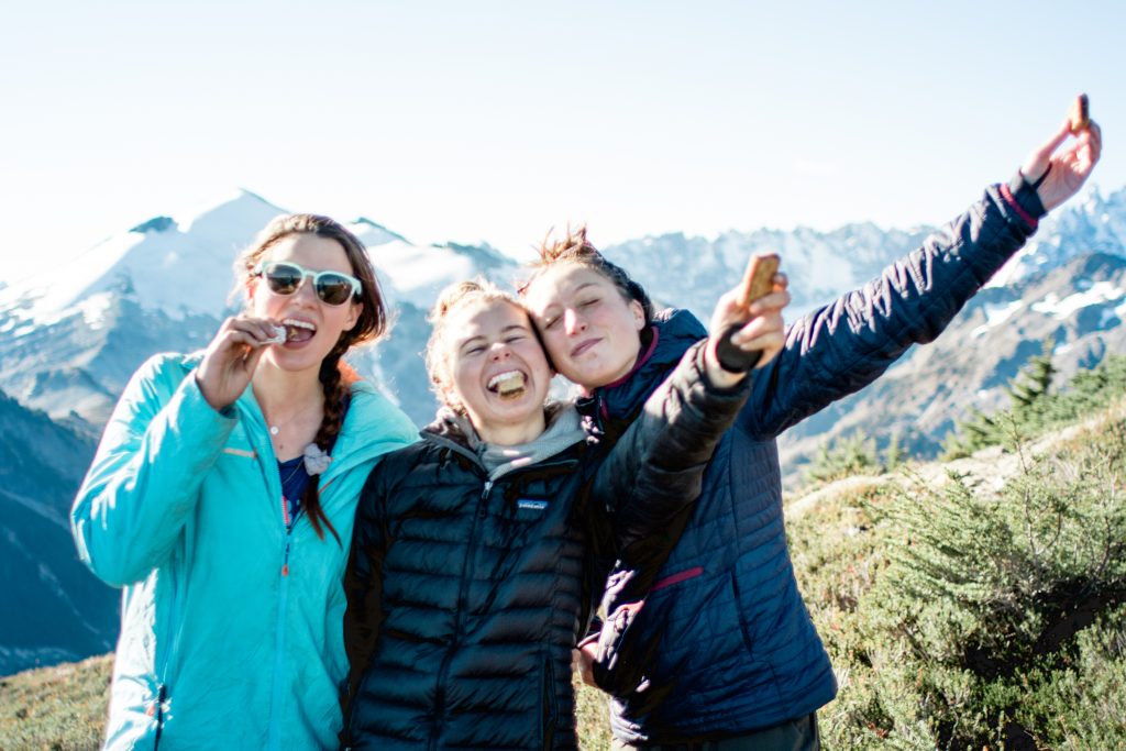 Three people who look happy pose with fig bars on top of a mountain vista. hiking snacks photo.