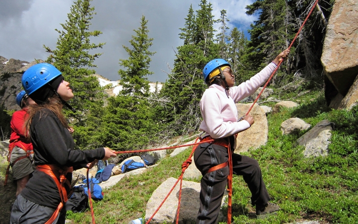 Three people wearing safety gear stand at the bottom of a rock wall and belay climbers.