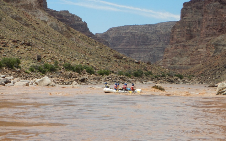 A group of students paddle a raft on a river framed by tall canyon walls