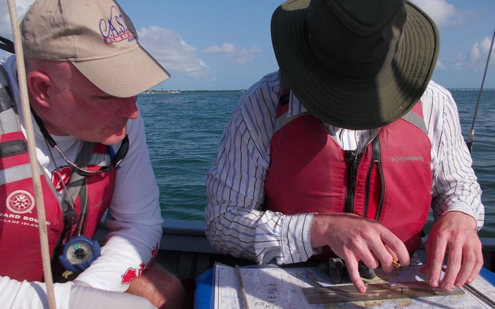 Two people wearing life jackets sit in a boat and examine a map.