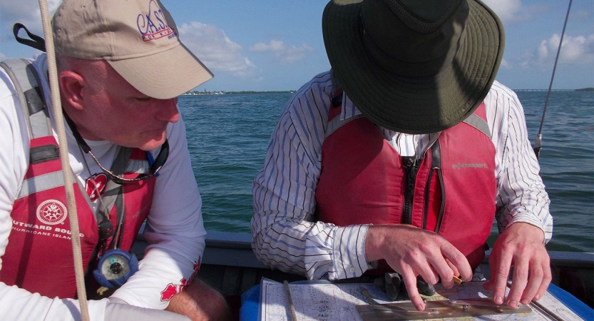 Two people wearing life jackets sit in a boat and examine a map.