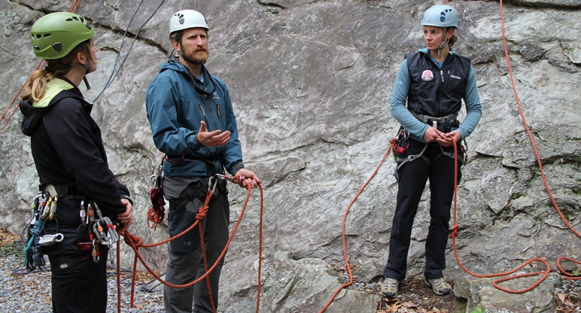 three people wearing safety gear are attached to ropes as they stand at the bottom of a rock face