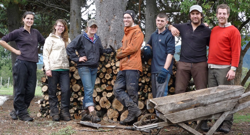 A group of people smile for a photo in front of a stack of wood. 