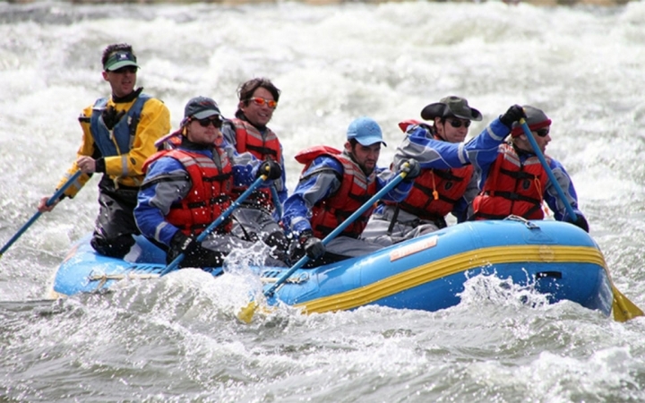 A group of people wearing safety gear paddle a raft through whitewater.