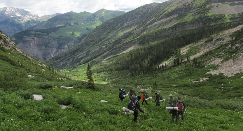 A group of people hike in a green valley surrounded by mountains.