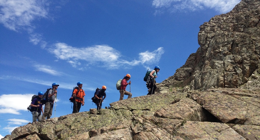 A group of people hike along a rocky ridge under a blue sky