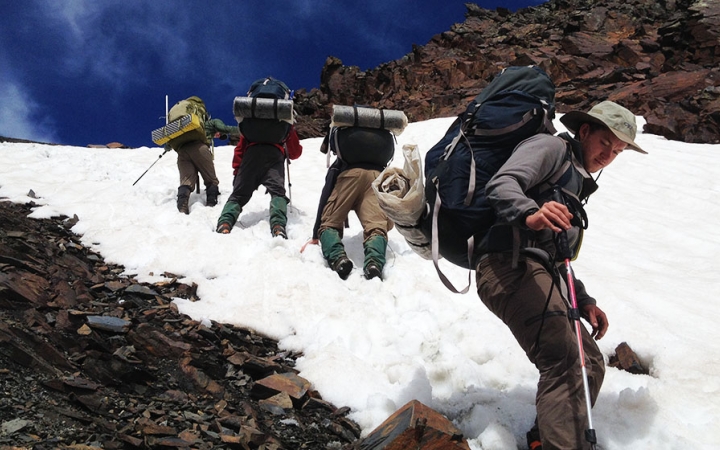 A group of people wearing backpacks make their way up a snowy incline.