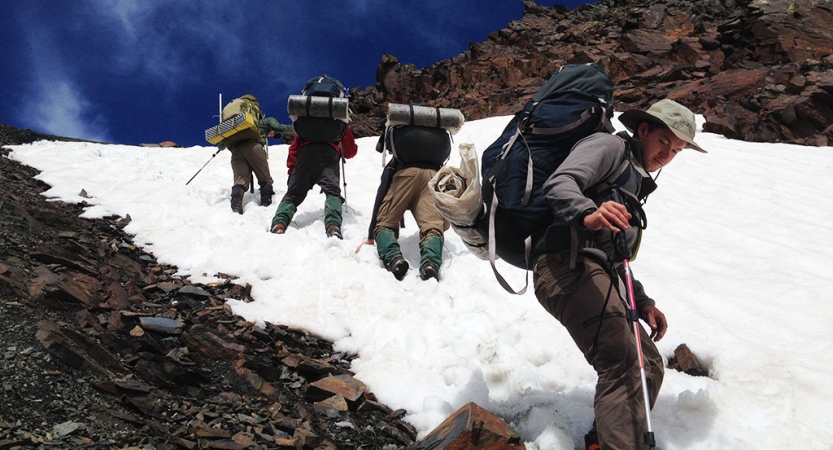 A group of people wearing backpacks make their way up a snowy incline.