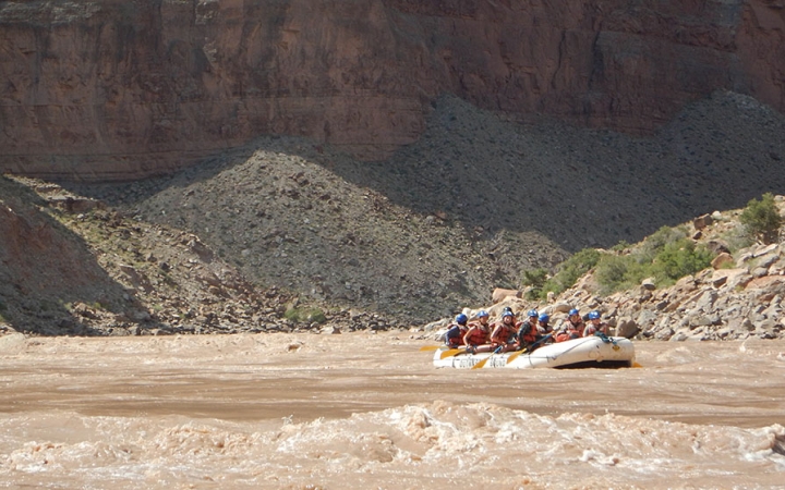 A group of people navigate a raft on a river sided by tall canyon walls