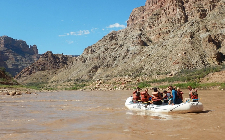 A group of people navigate a raft on a river sided by tall canyon walls