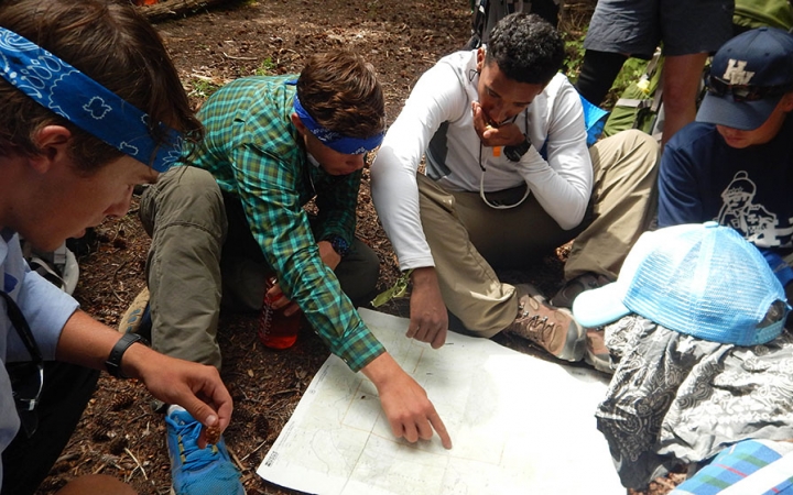 a group of people examine a map that is spread out on the ground