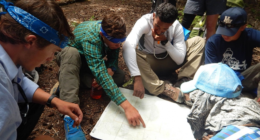 a group of people examine a map that is spread out on the ground