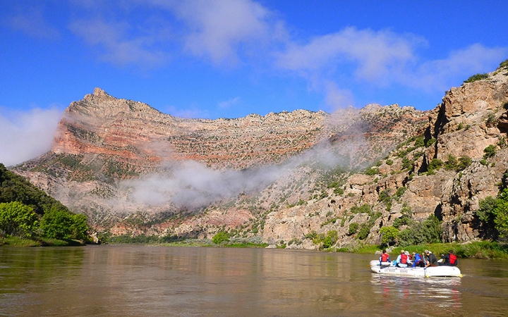 Students paddle a raft on a calm river in a desert landscape. 