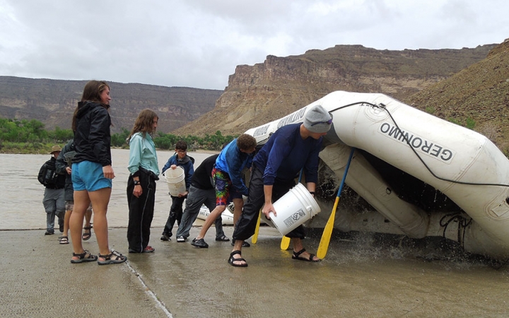 Using paddles, a raft is propped up upside down. A group of people use buckets to clean out the inside of the raft. 