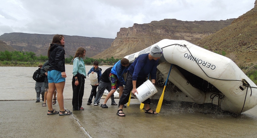 Using paddles, a raft is propped up upside down. A group of people use buckets to clean out the inside of the raft. 