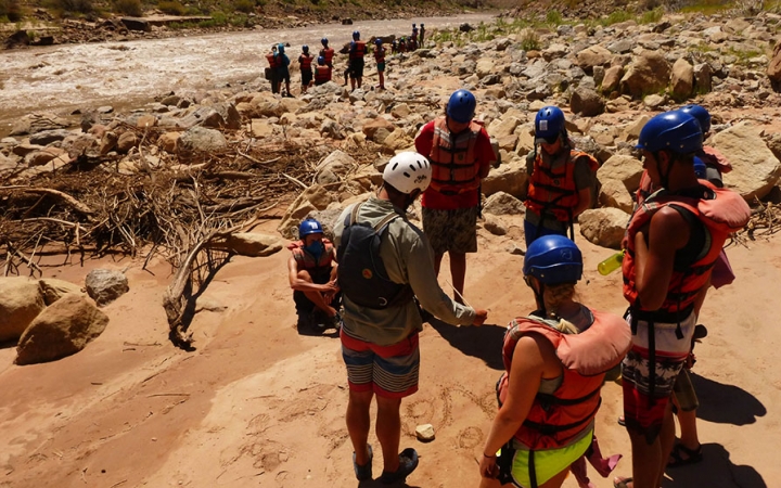 A group of students hike through a desert landscape toward a river.