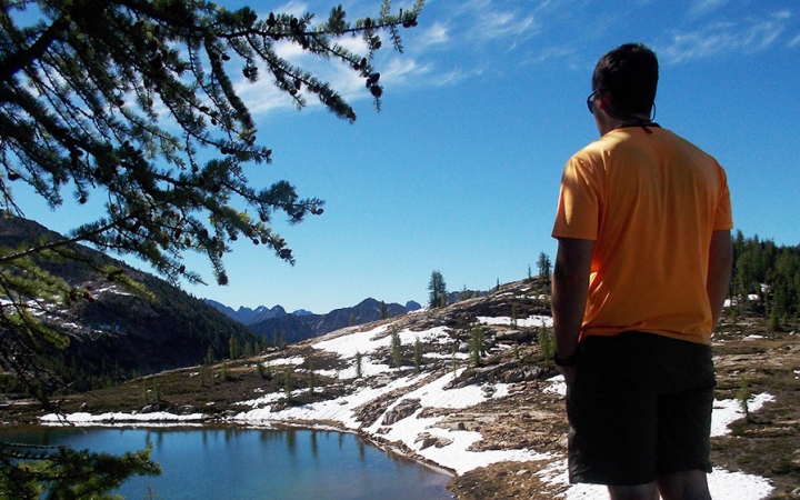a person looks out over an alpine lake with snow on the banks
