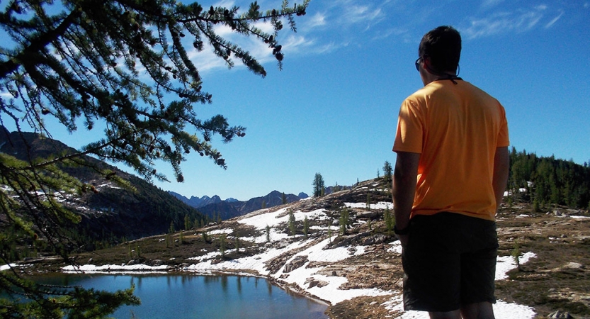 a person looks out over an alpine lake with snow on the banks