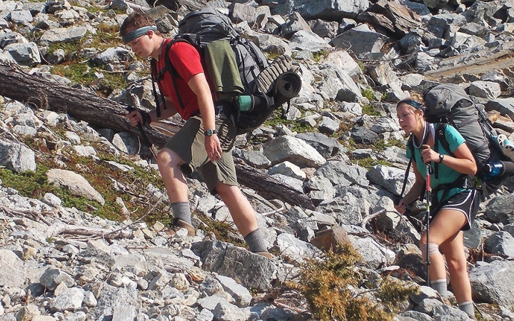 two people make their way up a rocky landscape on an outward bound trip