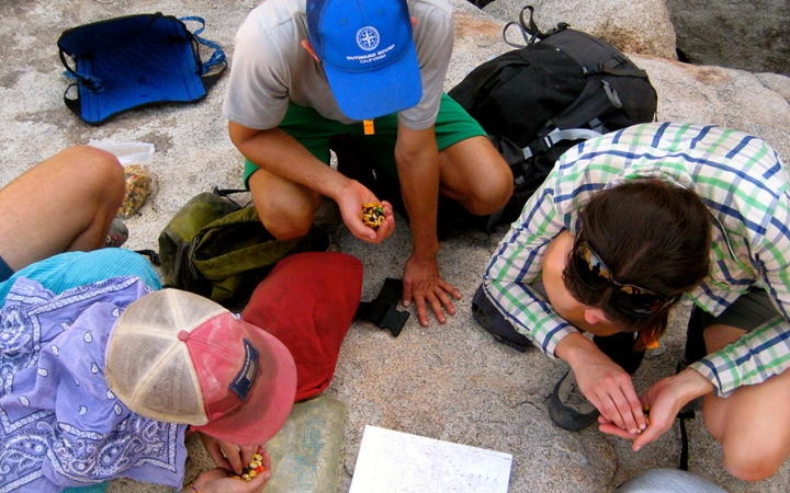 Three people rest and eat snacks as they examine a map on the ground. 