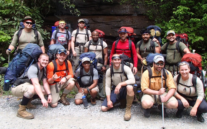 A group of veterans wearing backpacks pose for a photo on an outward bound trip.