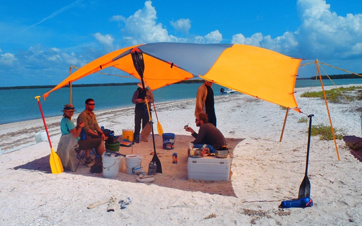 a group of veterans sits under a shelter on a beach during an outward bound course