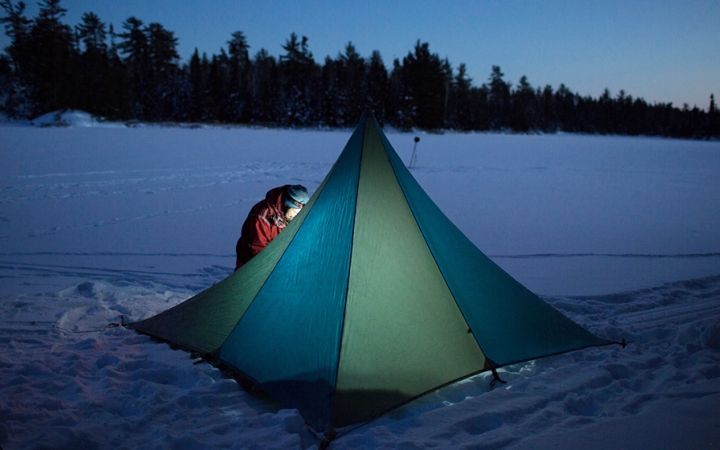 a tent resting on a snowy landscape is illuminated by a person's headlamp
