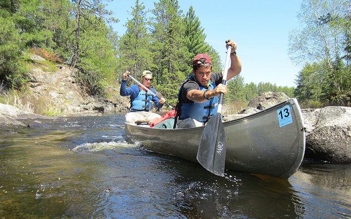 two gap year students paddle a canoe  between rocks