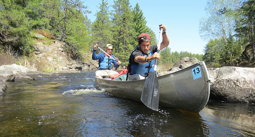 two gap year students paddle a canoe  between rocks